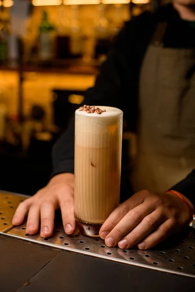 Primo piano di vetro con cocktail panna montata sul bar e mano maschile lo tiene — Foto Stock