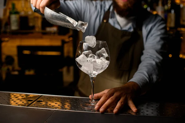 Klares Weinkelchglas, in das Barkeeper vorsichtig Eiswürfel aus einer Schaufel gießt — Stockfoto