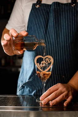 Erkek eli, küçük bir şişeden alkollü bir içeceği tahta süslemeli bir bardağa doldurur.