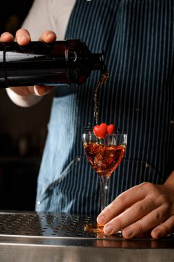Barmenin şişeden içki doldurduğu bir kalple dekore edilmiş bir şarap kadehinin önü.