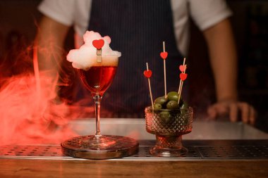 Kırmızı böğürtlen ve yeşil zeytinlerle süslenmiş köpüklü şarap kadehinin önünde.