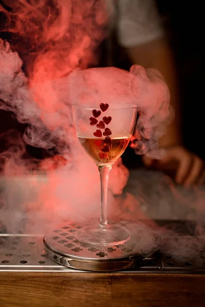 Бокал вина с напитком, украшенный красными сердцами стоит на баре и курить вокруг — стоковое фото