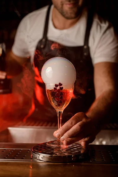 Barista mano maschile tiene bicchiere da vino con bevanda decorata con cuori e con bolla d'aria fumosa — Foto Stock
