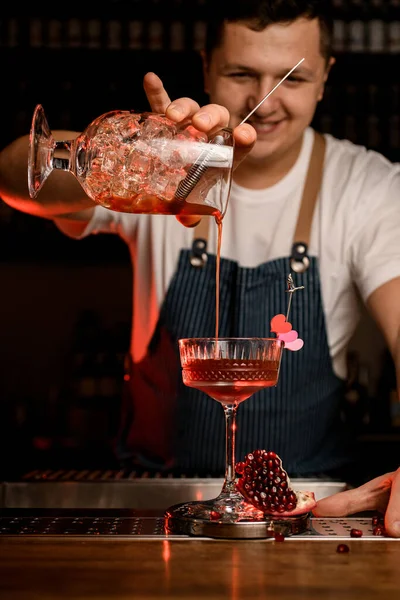 Mano del camarero sostiene la taza de mezcla con cóctel y hábilmente lo vierte en la copa de vino — Foto de Stock