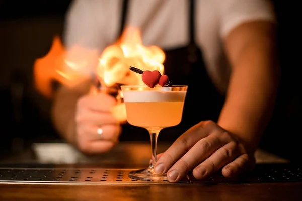 Splendida vista sul cuore decorativo su vetro con cocktail schiumoso sullo sfondo di fiamma ardente — Foto Stock