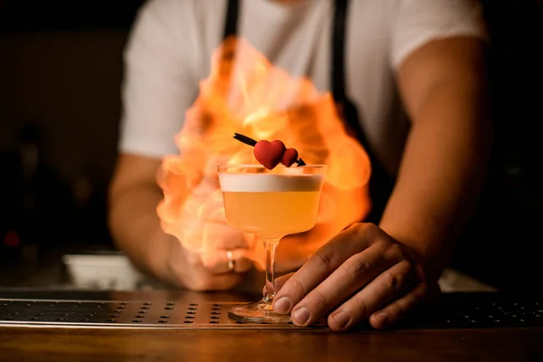 Прекрасный вид на декоративное сердце на стекле с пенным коктейлем на фоне огненного пламени — стоковое фото