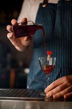 Erkek eli küçük bir şişeden alkollü bir içeceği süslemeli bir bardağa doldurur.