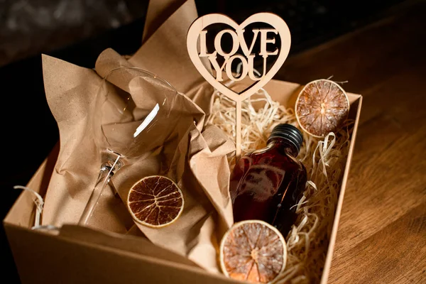 Yakın çekim cam ve küçük şişe içki ve karton kutuda dekoratif ahşap kalp — Stok fotoğraf