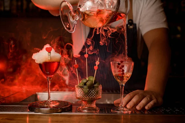 Na barze znajduje się szklanka z napojem i pianką oraz wazon z oliwkami i szkłem, do którego barman nalewa napój — Zdjęcie stockowe