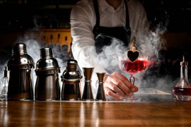 Siyah önlüklü barmen elinde kırmızı, lezzetli, alkollü kokteyl tutuyor.