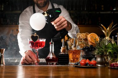 Barmen elinde kırmızı alkollü kokteyl tutuyor ve dumanlı hava balonu yapıyor.
