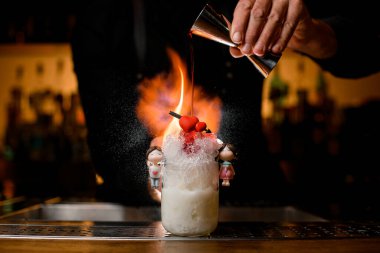 Barmen elinde çeliği tutuyor ve ustalıkla kokteyl bardağını şurupla dolduruyor.