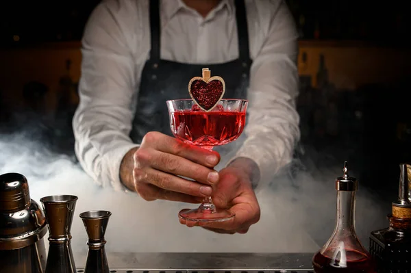 Barman segurando em mãos vidro de cristal de bebida alcoólica vermelha — Fotografia de Stock