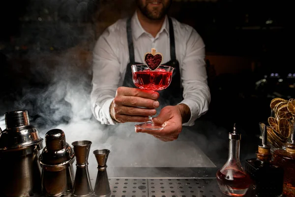 Usmívající se barman drží v ruce křišťálovou sklenici červeného alkoholického nápoje — Stock fotografie