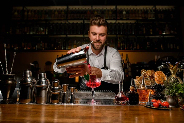 Barman sorridente com barba derramando bebida alcoólica vermelha fresca em vidro — Fotografia de Stock