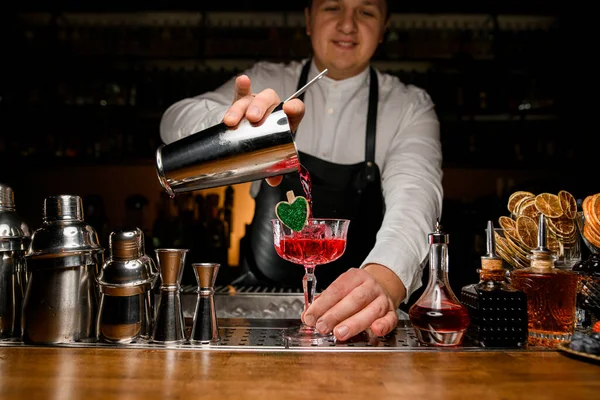 Uśmiechnięty mężczyzna barman starannie wlewa czerwony świeży napój alkoholowy do szklanki — Zdjęcie stockowe