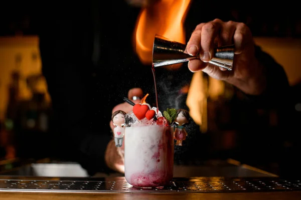 Barman houdt stalen jigger in zijn hand en giet siroop netjes in glas met cocktail versierd met kleine harten en paar. — Stockfoto