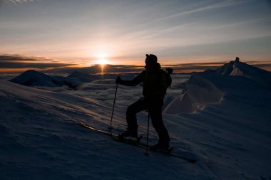 Gökyüzü ve güneşin doğuşuna karşı bir kayakçının silueti