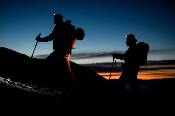 Крупный план силуэтов лыжников, взбирающихся на гору на фоне вечернего неба — стоковое фото