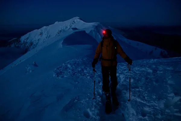 Visão noturna do esquiador caminhando ao longo da trilha no cume da montanha nevada — Fotografia de Stock