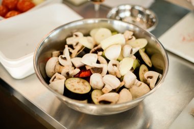 Çelik kaseye yakın plan doğranmış şampiyon mantarları ve sebzelerle.