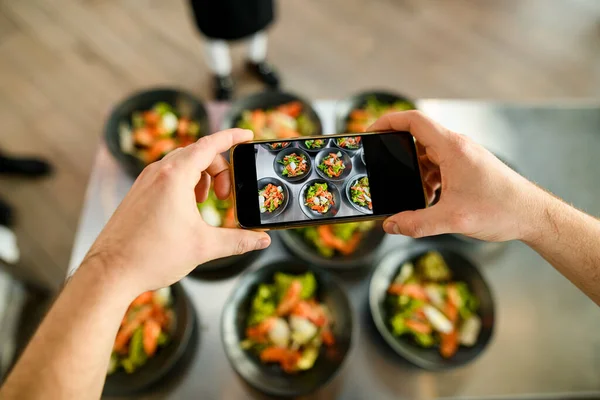 Smartphone in male hands on which plates with delicious salad are photographed — Stock Photo, Image