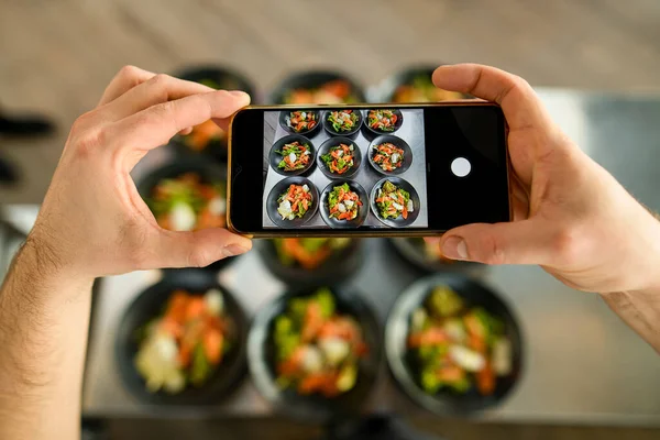 Selective focus on a smartphone in male hands, on which plates with delicious salad are photographed — Stock Photo, Image