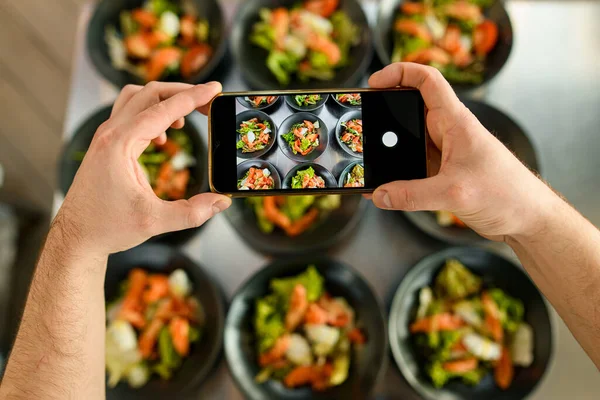 Male hands holds smartphone and make photo of plates with delicious salad — Stock Photo, Image