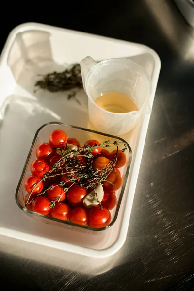 Vista superior sobre tomates rojos pequeños y ramitas de verduras en un tazón cuadrado transparente —  Fotos de Stock