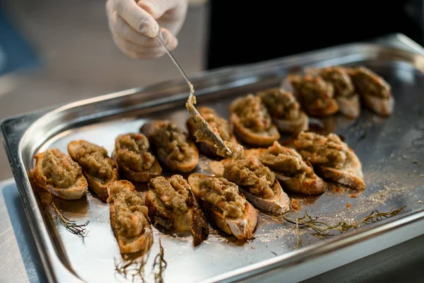 Ręka szefa kuchni rozprzestrzenia się przez łyżkę mieszanki warzyw na plasterkach bagietki na tacy — Zdjęcie stockowe