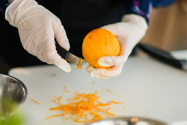 Руки в перчатках держит апельсин и отрезает кожуру от него — стоковое фото