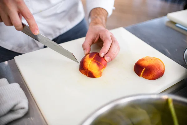 Вид персика нарезанного на разделочной доске и мужской руки шеф-повара с ножом рядом — стоковое фото