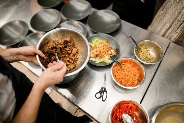 Şefin elleri ahtapot dolu kaseleri ve diğer malzemelerle dolu kaseleri tutuyor.