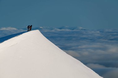 Beyaz, karlı dağ yamacının tepesinde kayakçılar var.