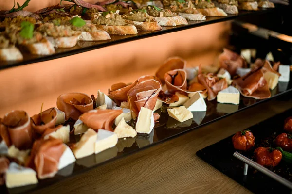 Various types of appetizers. Selective focus on pieces of brie cheese and prosciutto and salami — Stock Photo, Image