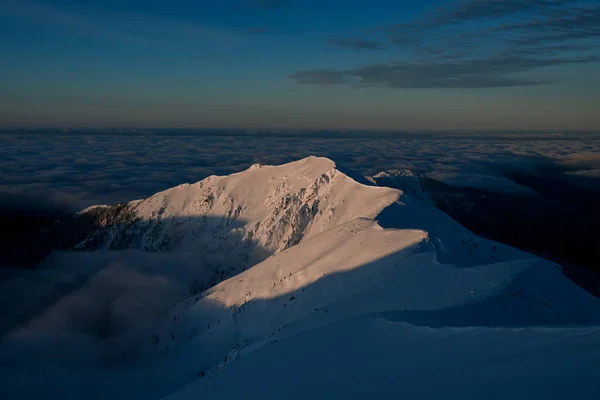 Aerial view of the snow-covered mountain range surrounded by clouds against background of sky — 图库照片