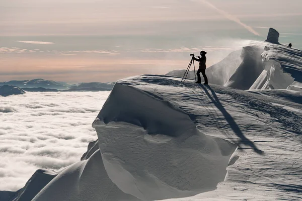 Fotografo con macchina fotografica su treppiede in piedi su pendio coperto di neve bianca. — Foto Stock