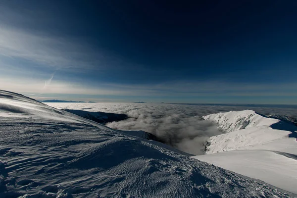 Amazing high view of the snow-covered mountain range surrounded by clouds and clear blue sky — Fotografia de Stock