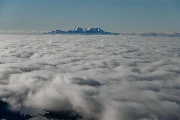 Prachtig uitzicht op witte kruipende nevelige wolken en besneeuwde bergtoppen — Stockfoto