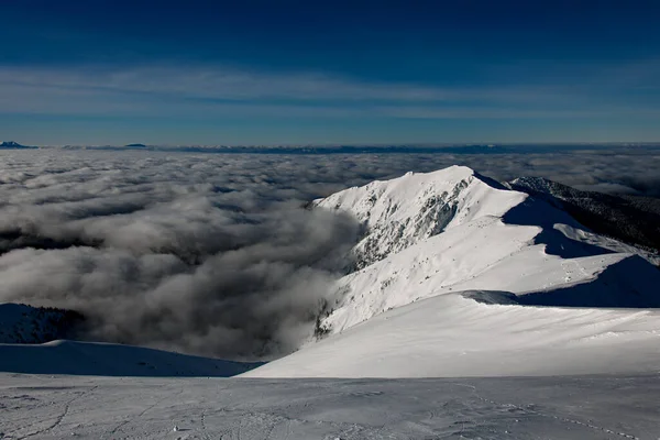 Glorious view of the snow-covered mountain range surrounded by clouds and clear blue sky — Fotografia de Stock