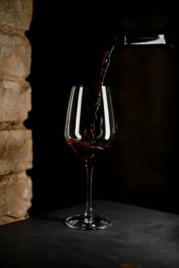 Kırmızı şarabın şişeden döküldüğü harika bir şarap kadehi manzarası..