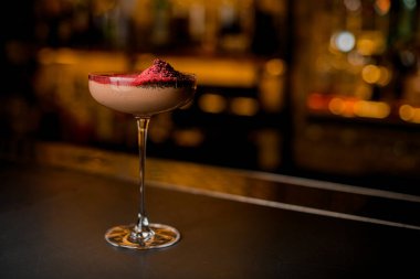 Barın arka planında toz ile süslenmiş pembe içecekle süslenmiş cam.