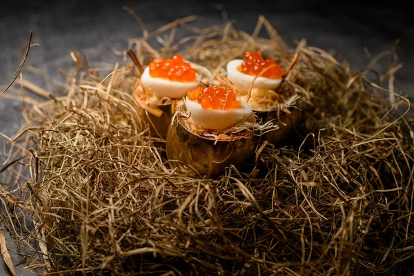Főtt tojás piros kaviárral töltve és arany héjban tálalva dekoratív szénán — Stock Fotó