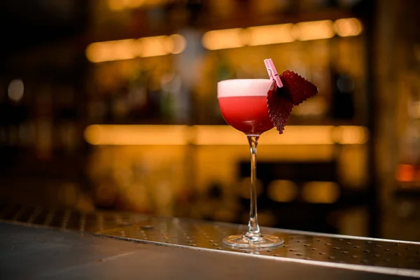 Bicchiere da cocktail con bevanda rosa brillante schiumosa e decorazione su sfondo bar sfocato — Foto Stock