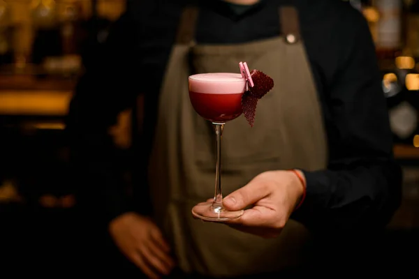 Main de barman tient verre à cocktail avec boisson rose mousse et décoration — Photo