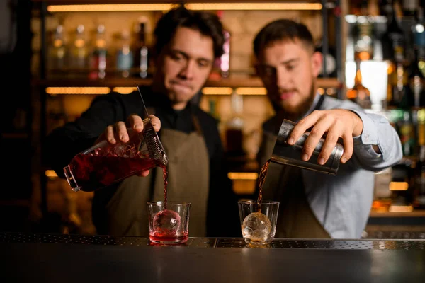 Dois copos com o gelo no qual os empregados de bar cuidadosamente vazam coquetéis diferentes — Fotografia de Stock