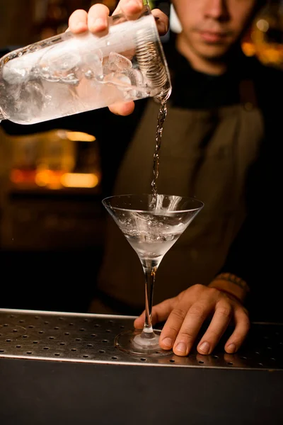 Main de barman masculin tient une tasse de mélange et verse un cocktail dans un verre de martini — Photo