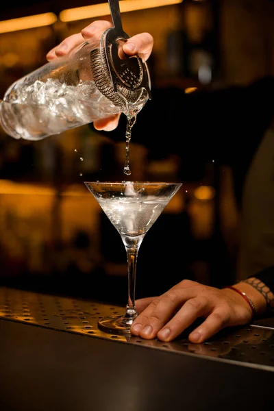 Mano di barman tiene una tazza di miscelazione e versa un cocktail in un bicchiere da martini — Foto Stock
