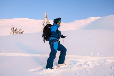 Sırt çantalı parlak bir kayakçı karın üzerinde duruyor.