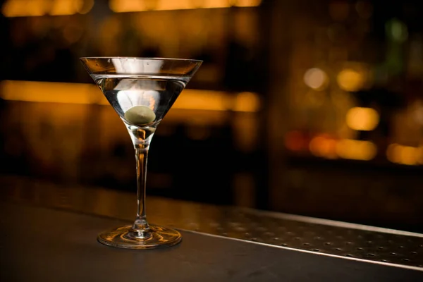 Бокал мартини с напитками и зеленой оливкой на барной стойке. Фон размытой полосы. — стоковое фото